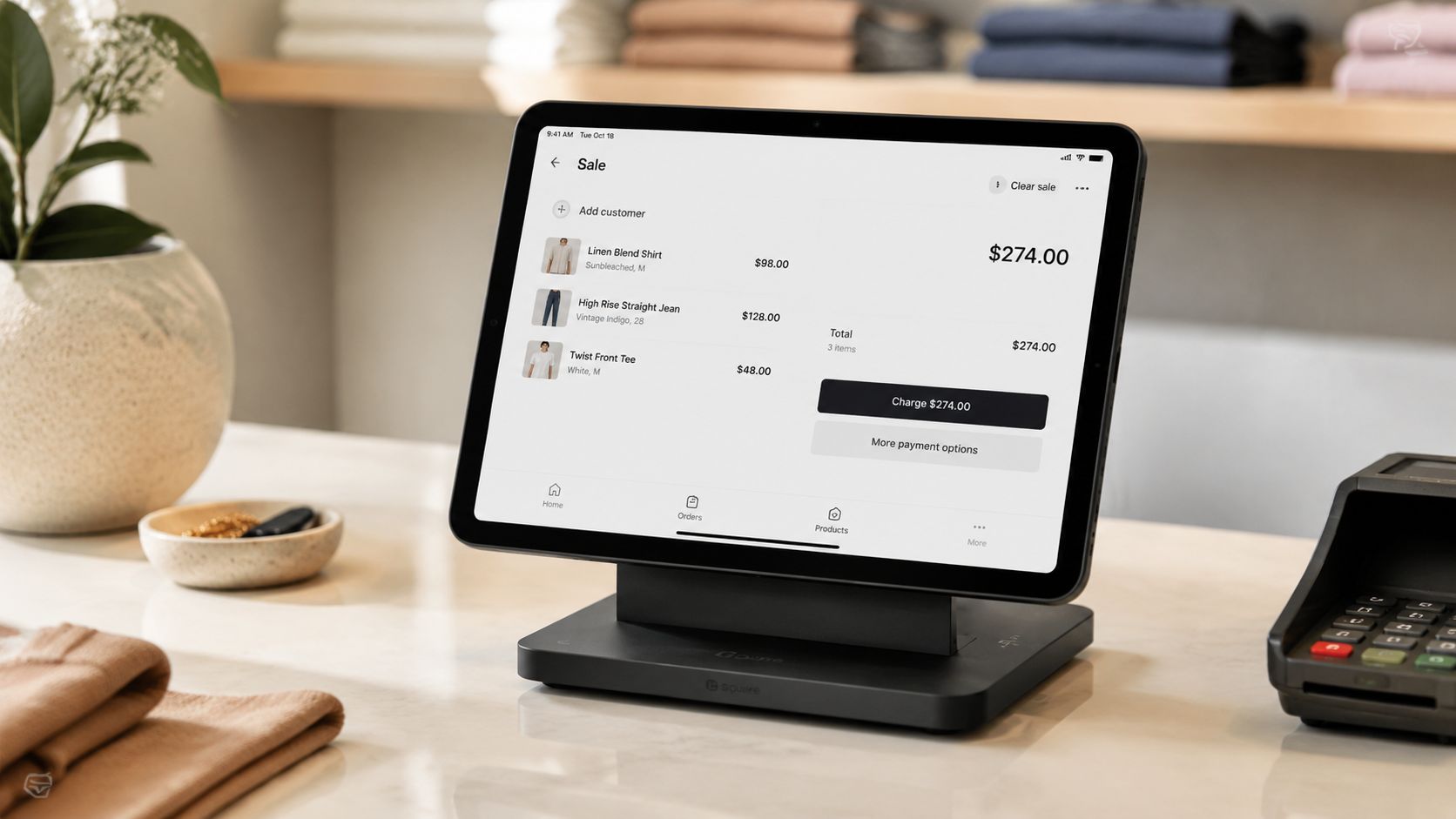 A modern touchscreen tablet point of sale system on a shop counter displaying a clothing store checkout screen.