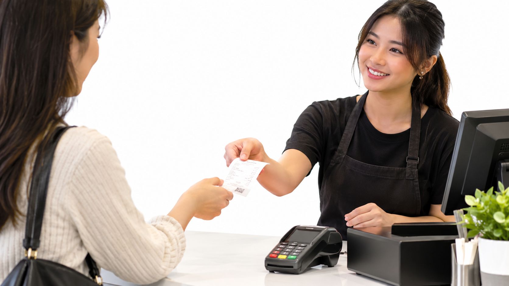 A friendly cashier handing a printed store receipt to a customer at a checkout counter.